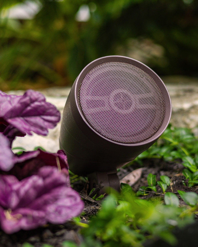 A close-up photo of a Sound by Vista outdoor speaker in a garden